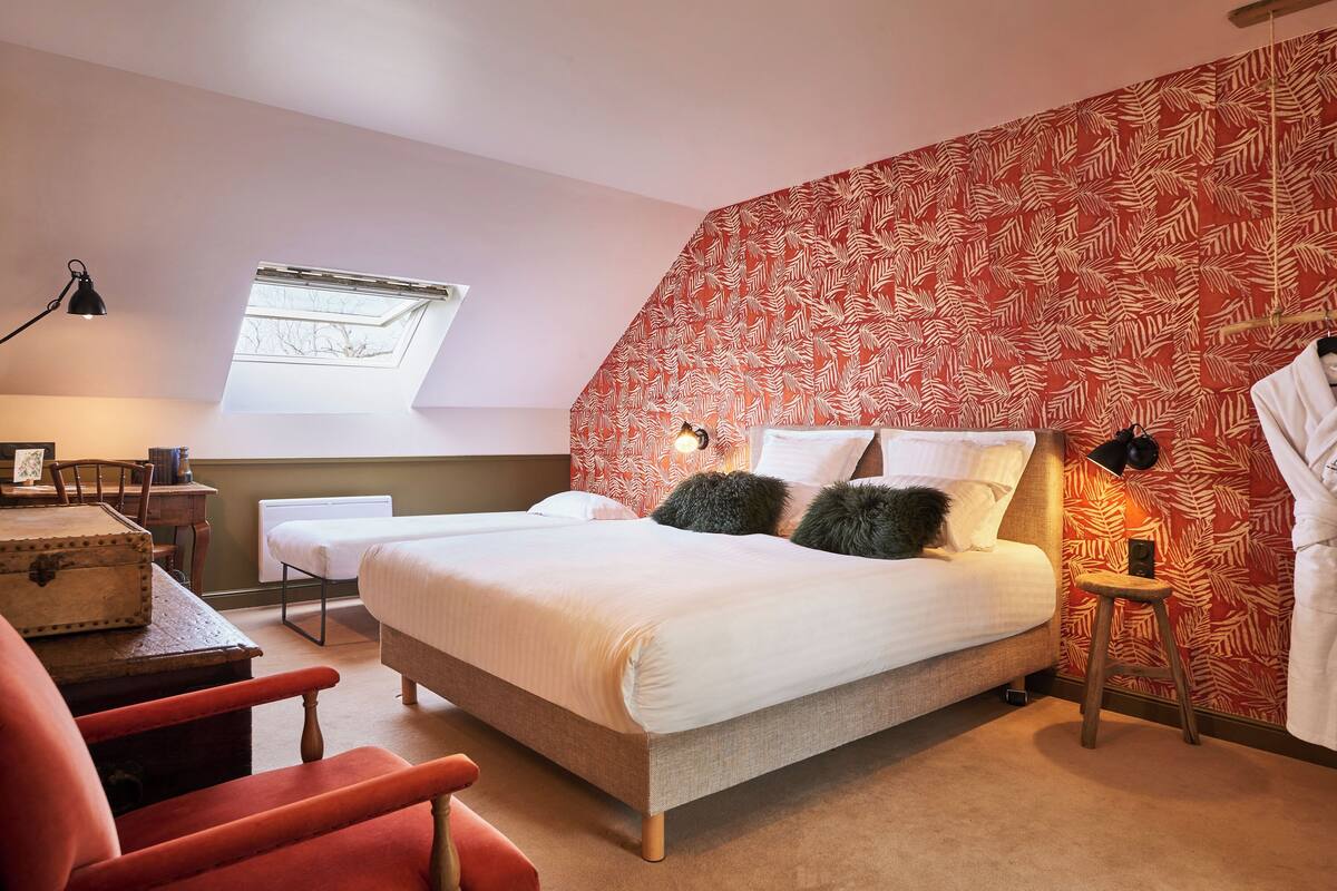 A bedroom with a bed, a desk, a chair, a window, and a patterned wall.