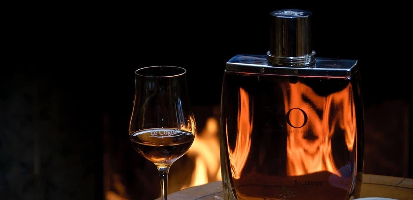 A bottle of Le Cognac and a glass of wine on a table.