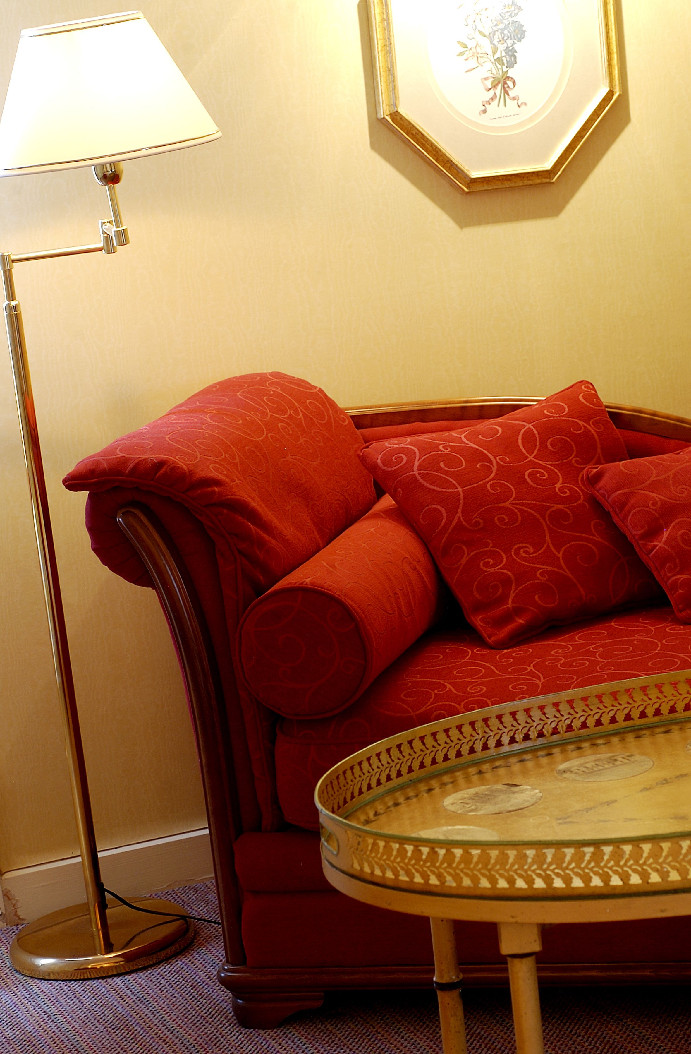 A red sofa with patterned cushions, a round glass coffee table, and a floor lamp.