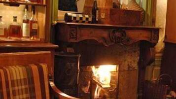 A cozy bar area with a fireplace, wooden furniture, and a variety of bottles.