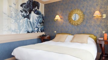 Quarto de hotel com uma cama grande, uma mesa de cabeceira, uma luminária na parede e um espelho com design de raios de sol.