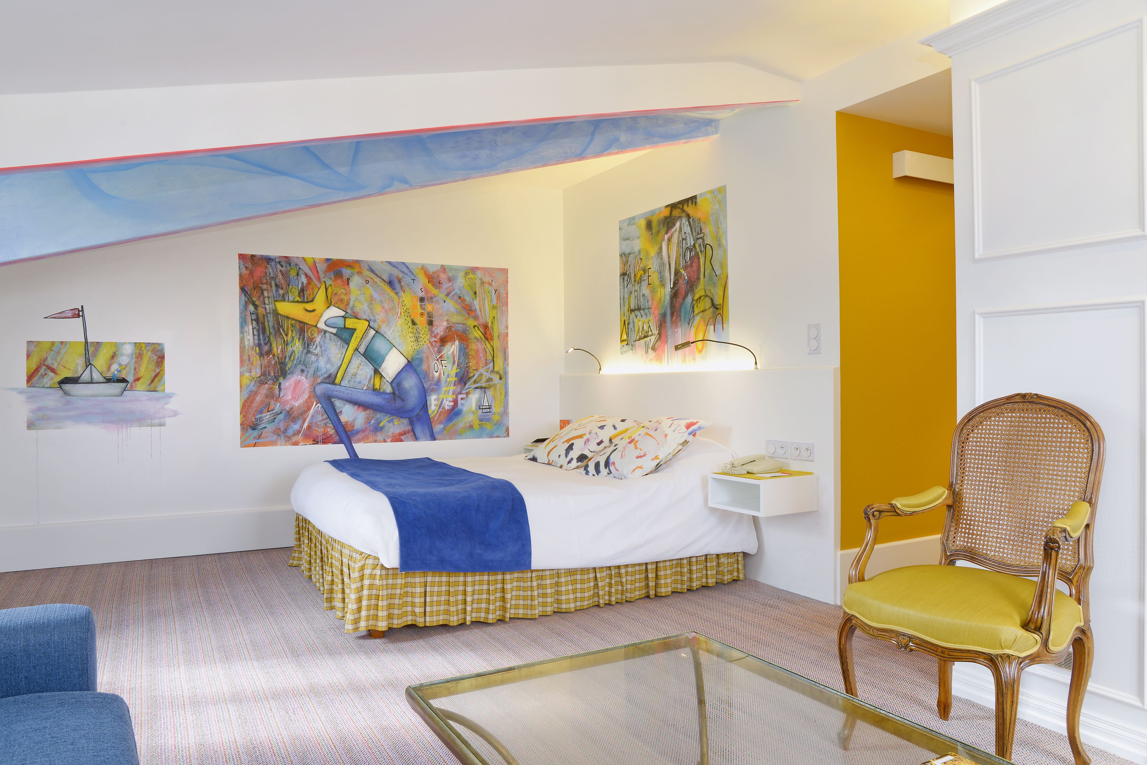 Een slaapkamer met een bed, een stoel en kunstwerken aan de muur.