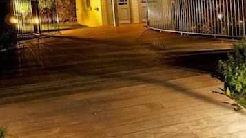 Une terrasse en bois menant à un bâtiment doté d’un porche couvert et d’une zone délimitée par une clôture.
