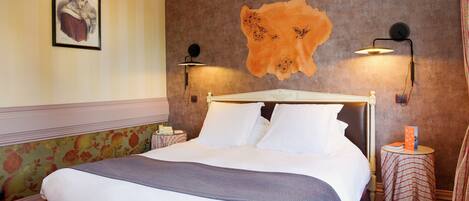 A neatly made bed with white linens and a gray throw, a framed picture on the wall, and two wall-mounted lamps.