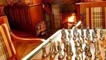 A chessboard in a warmly lit room with wooden furniture and a fireplace.