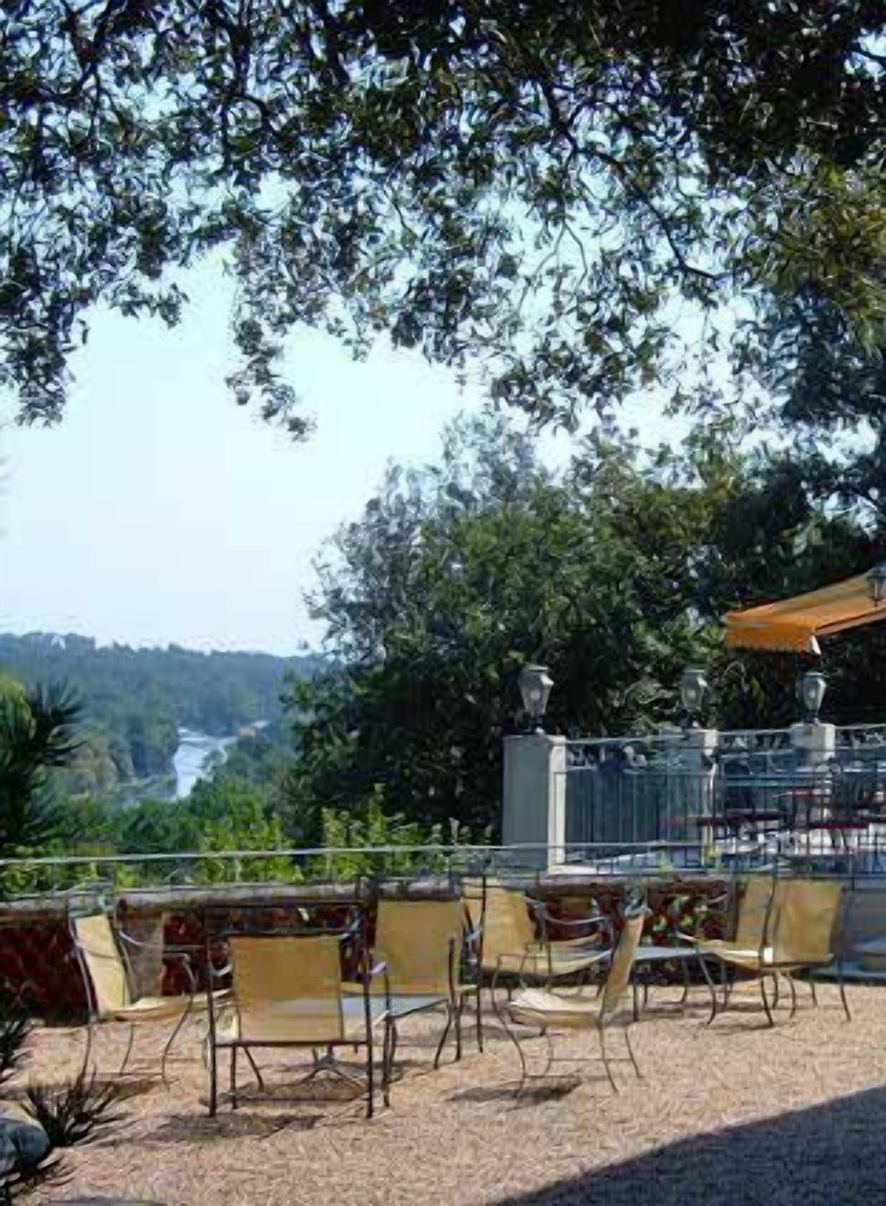 Een terras met stoelen en tafels, omringd door bomen en uitzicht op een rivier.