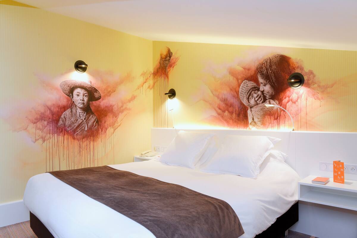 A hotel room with a large bed, a nightstand, and a wall mural.