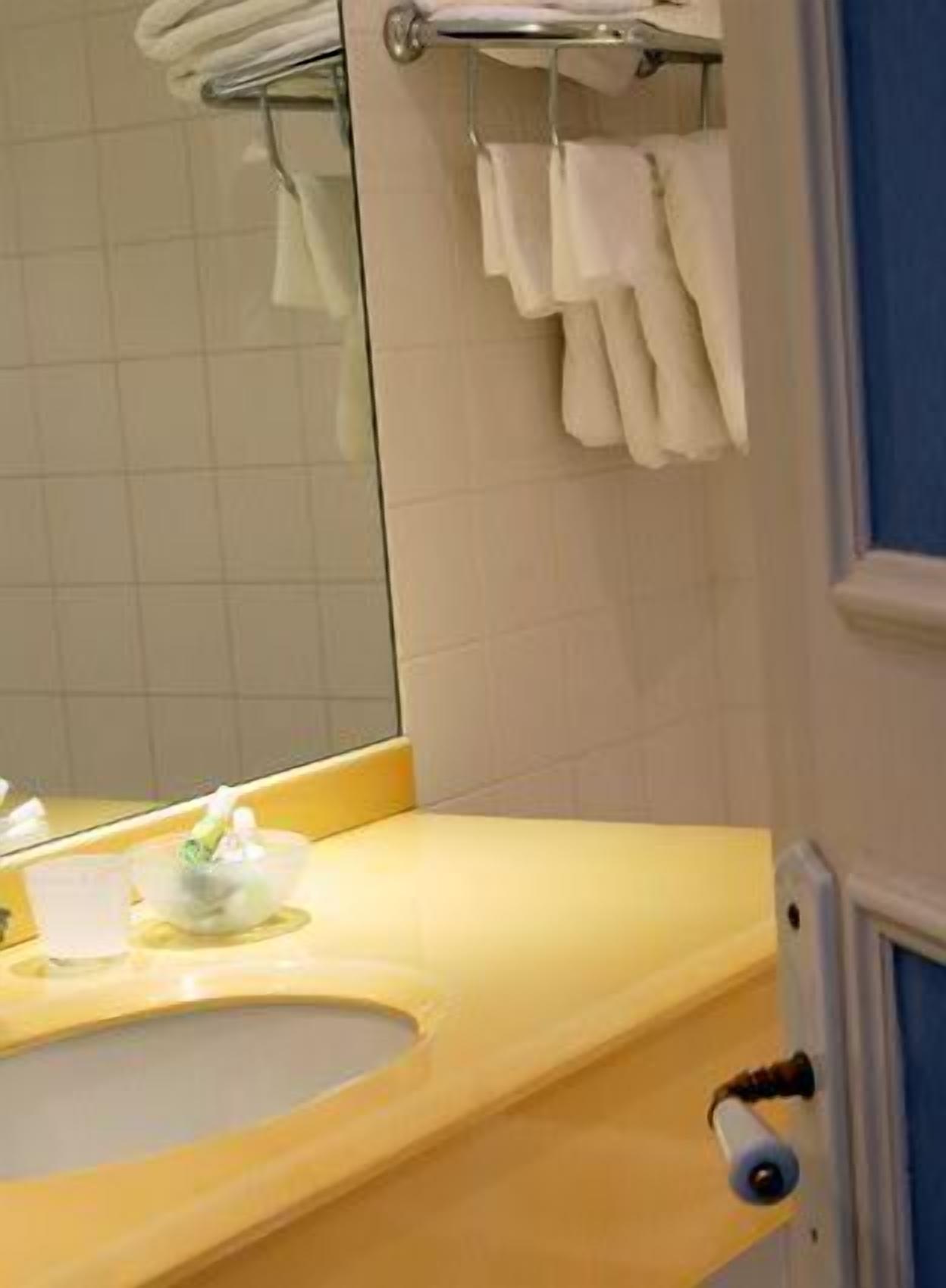 A bathroom with a yellow sink, a mirror, and a towel rack.