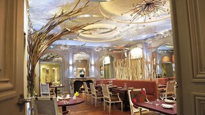 An opulent dining area with ornate chandeliers, a fireplace, and plush seating.