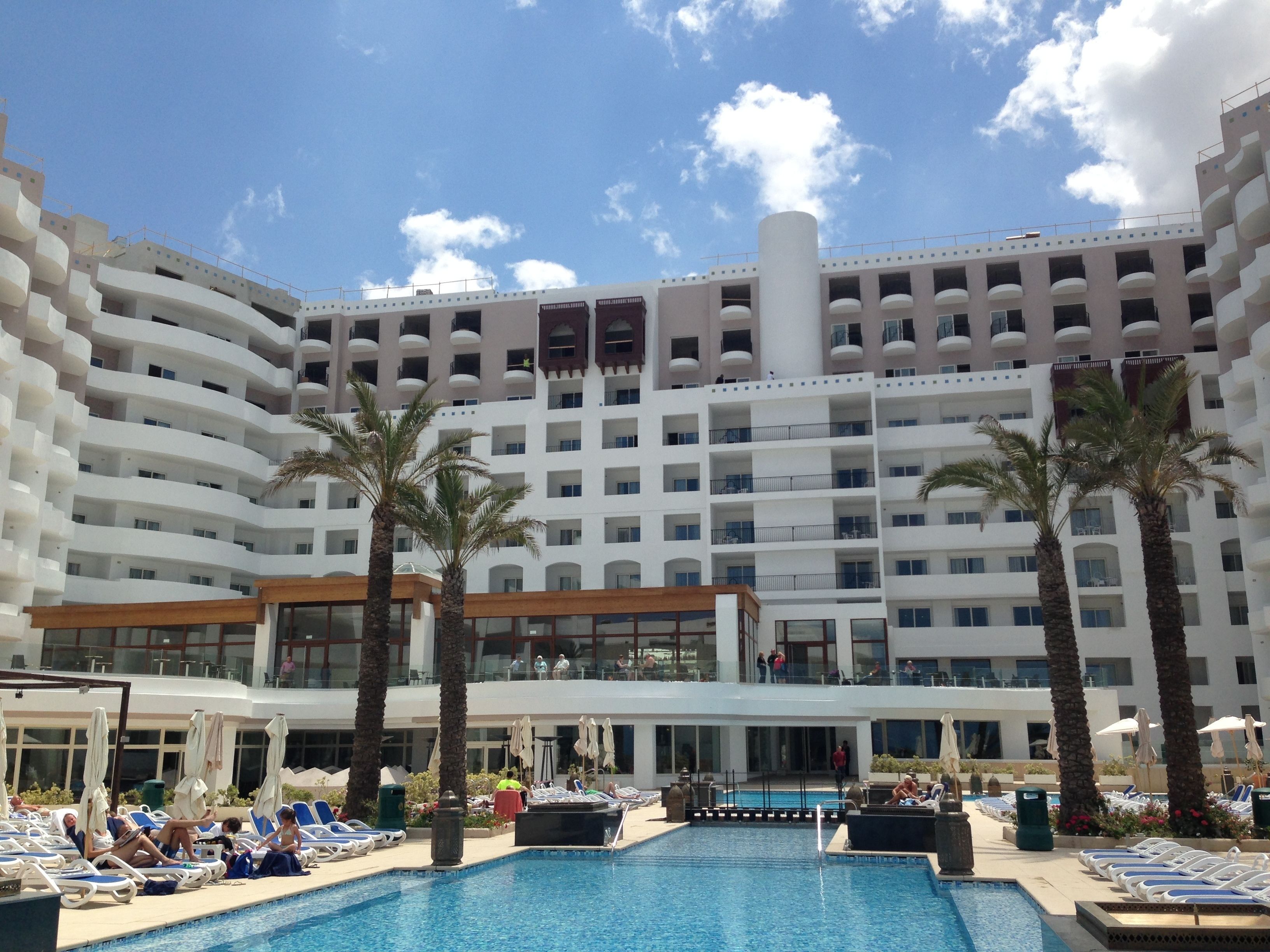 Un hôtel doté de nombreux balcons, d’une piscine et de palmiers.