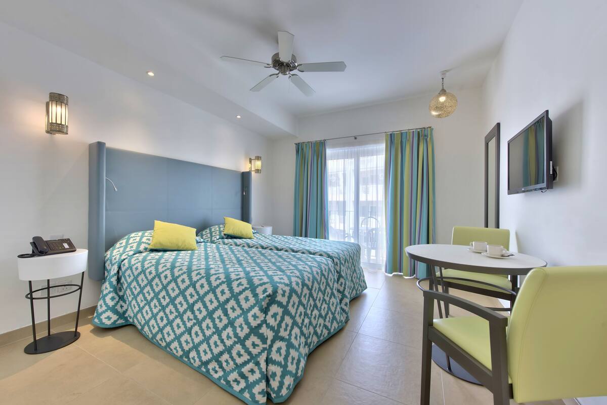 A hotel room with a bed, a desk, a chair, a TV, and a ceiling fan.