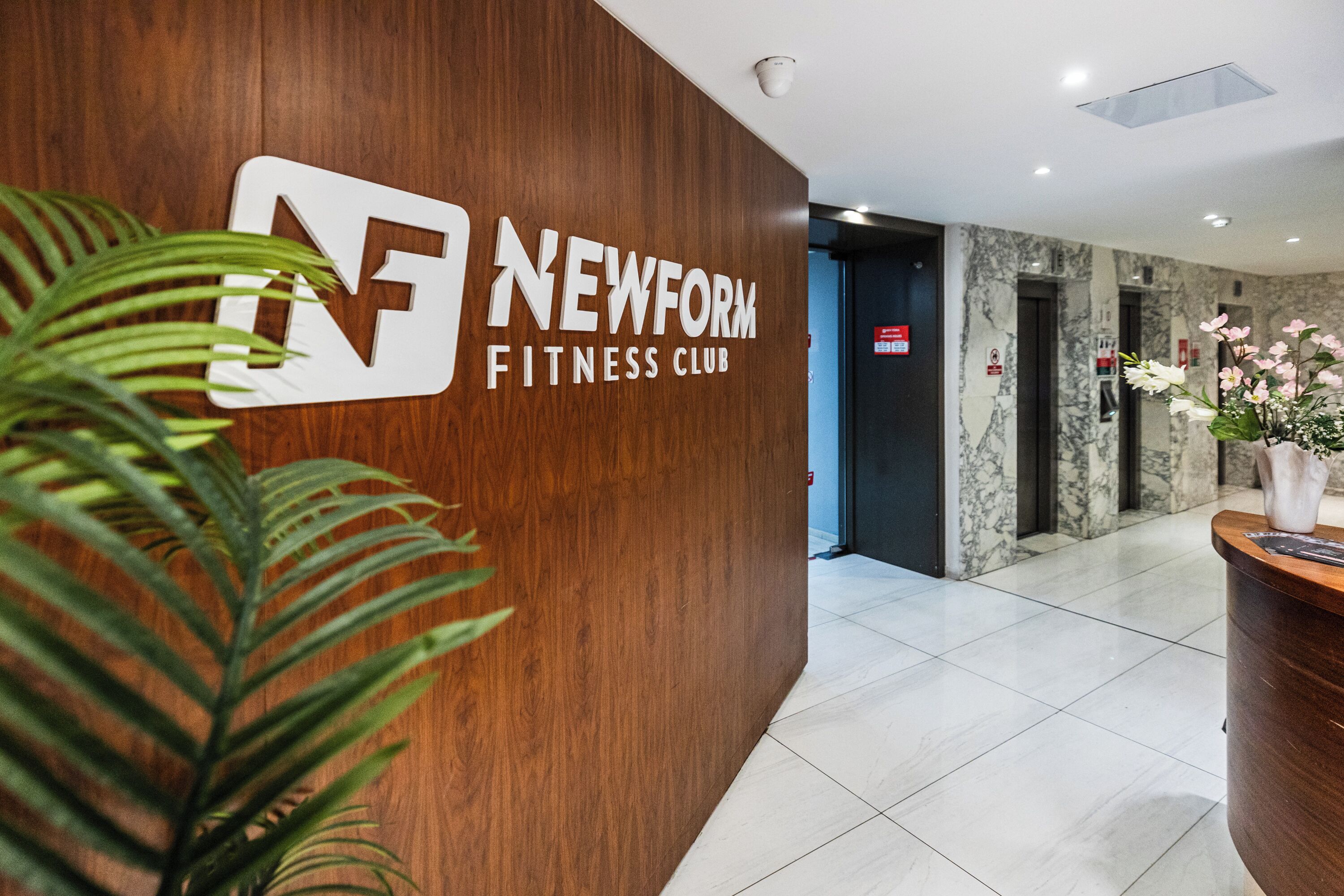 A reception area with a wooden wall, a logo, and a potted plant.