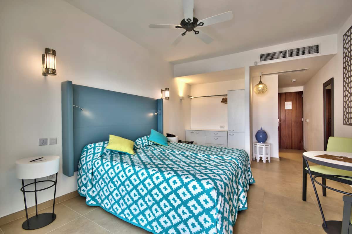 A bedroom with a bed, bedside table, ceiling fan, and a small dining area with a table and chair.