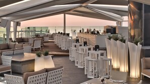 A rooftop bar with white furniture, a bar area, and a view of the ocean. - db San Antonio Hotel & Spa - All Inclusive (St. Paul's Bay)