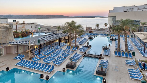 A rooftop pool area with multiple sun loungers, a small slide, and a view of the sea at sunset. - db San Antonio Hotel & Spa - All Inclusive (St. Paul's Bay)