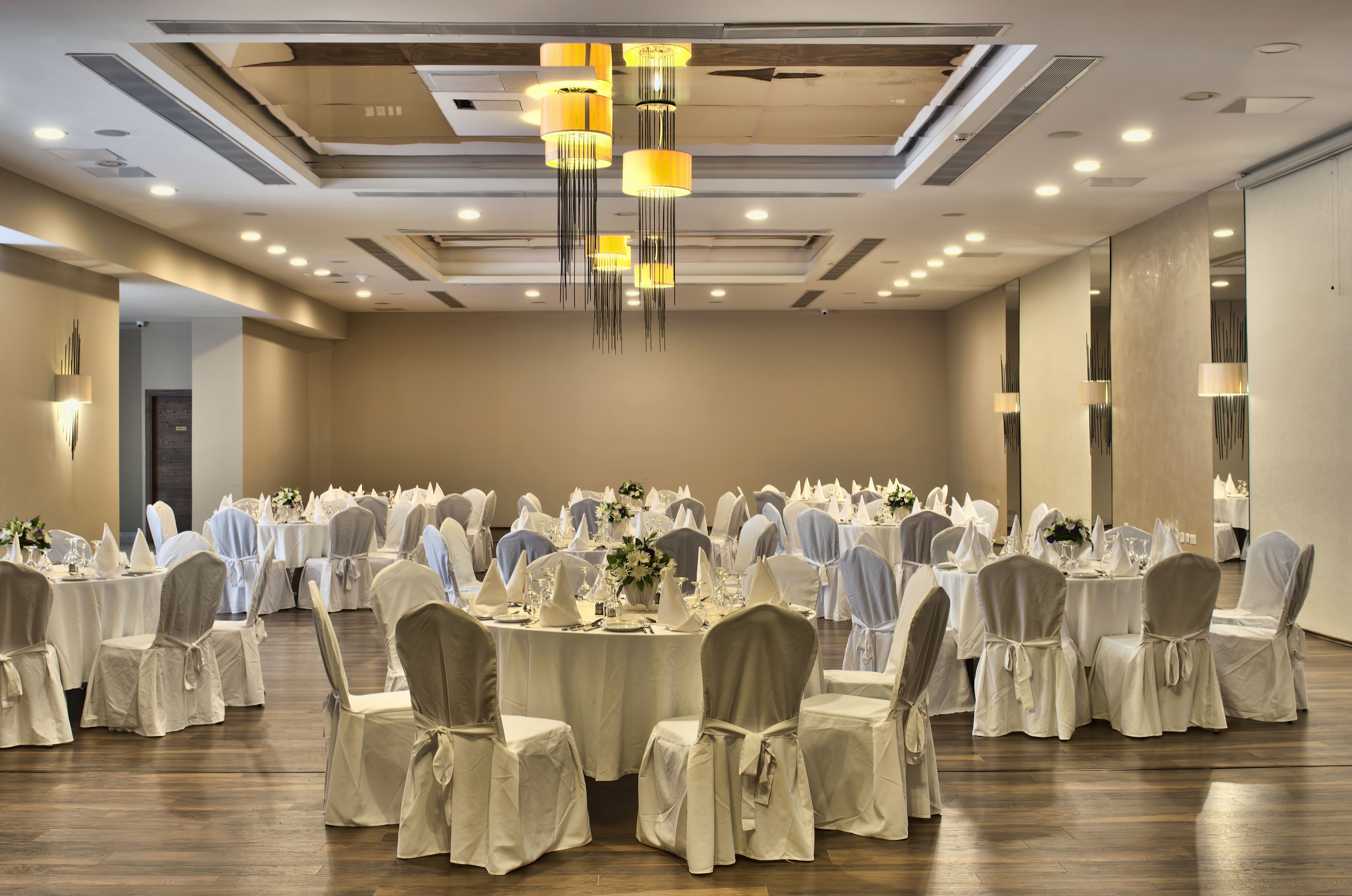 A banquet hall with round tables set for a formal event, featuring chandeliers and wall-mounted lighting.