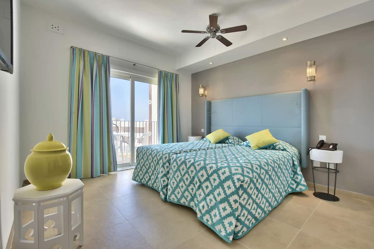 A bedroom with a bed, a ceiling fan, a bedside lamp, and a view of the outside.