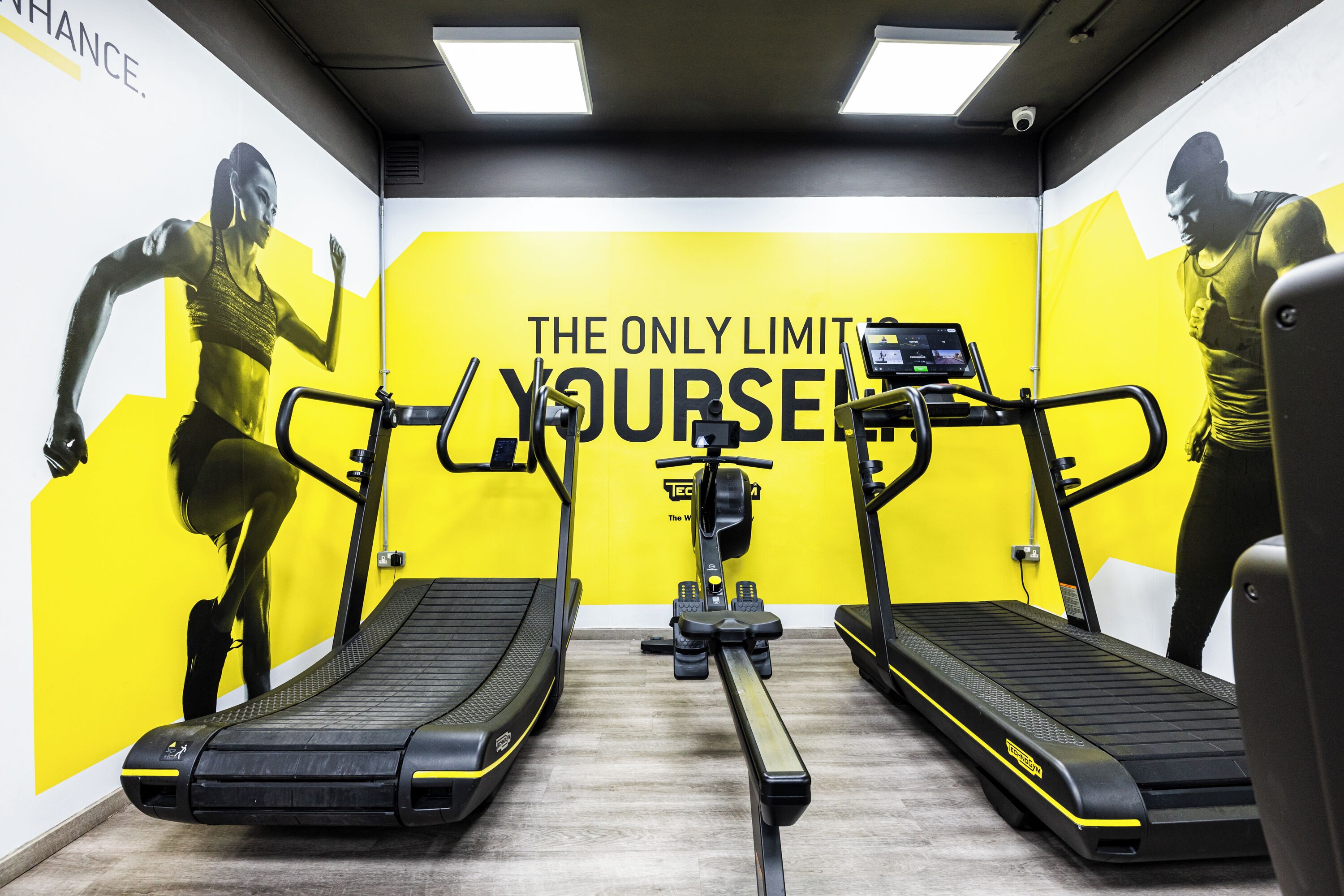 Ein Fitnessraum mit Laufbändern, Rudergerät und einer Wand mit motivierenden Texten.