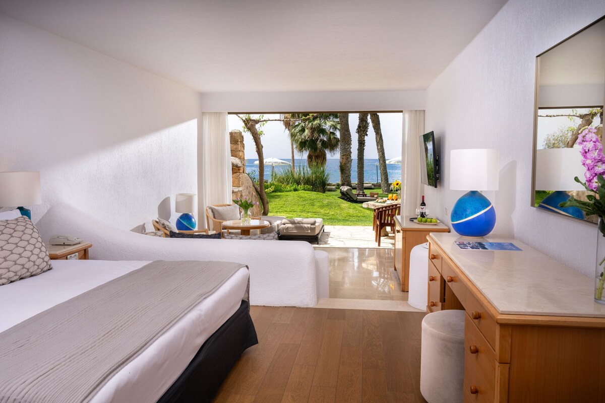 Een hotelkamer met een bed, bureau en uitzicht op de oceaan.
