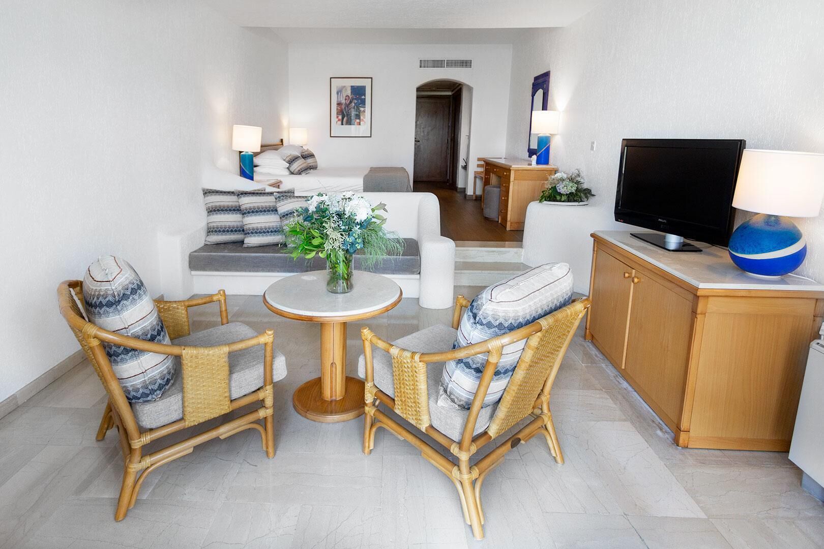 Un salon moderne comprenant un canapé, deux fauteuils en osier, une table ronde, un téléviseur et un meuble.