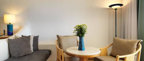 A room with a bed, a sofa, two chairs, a table, a lamp, and a vase with flowers.