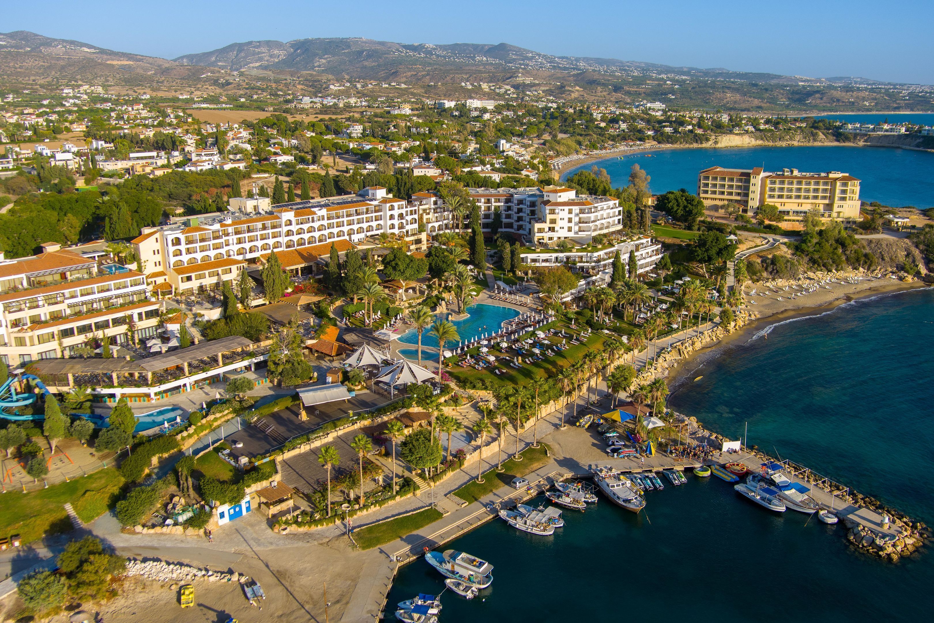 Vista aérea de um hotel à beira-mar, com vários edifícios, uma marina e uma praia.