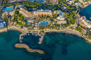 An aerial view of a coastal hotel with multiple buildings, a marina, and a large swimming pool.