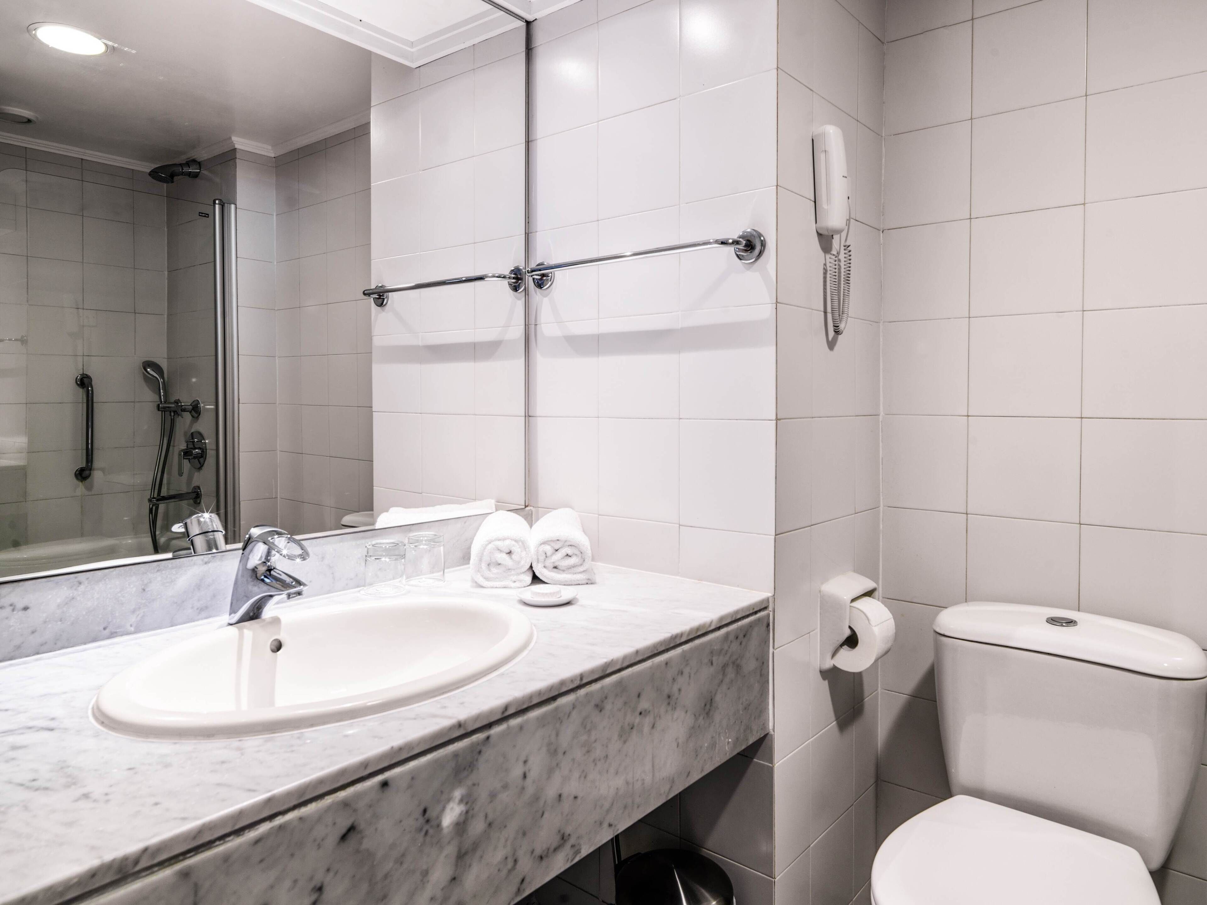 Un baño moderno con lavamanos de mármol, cabina de ducha con mampara de vidrio, inodoro y secamanos.