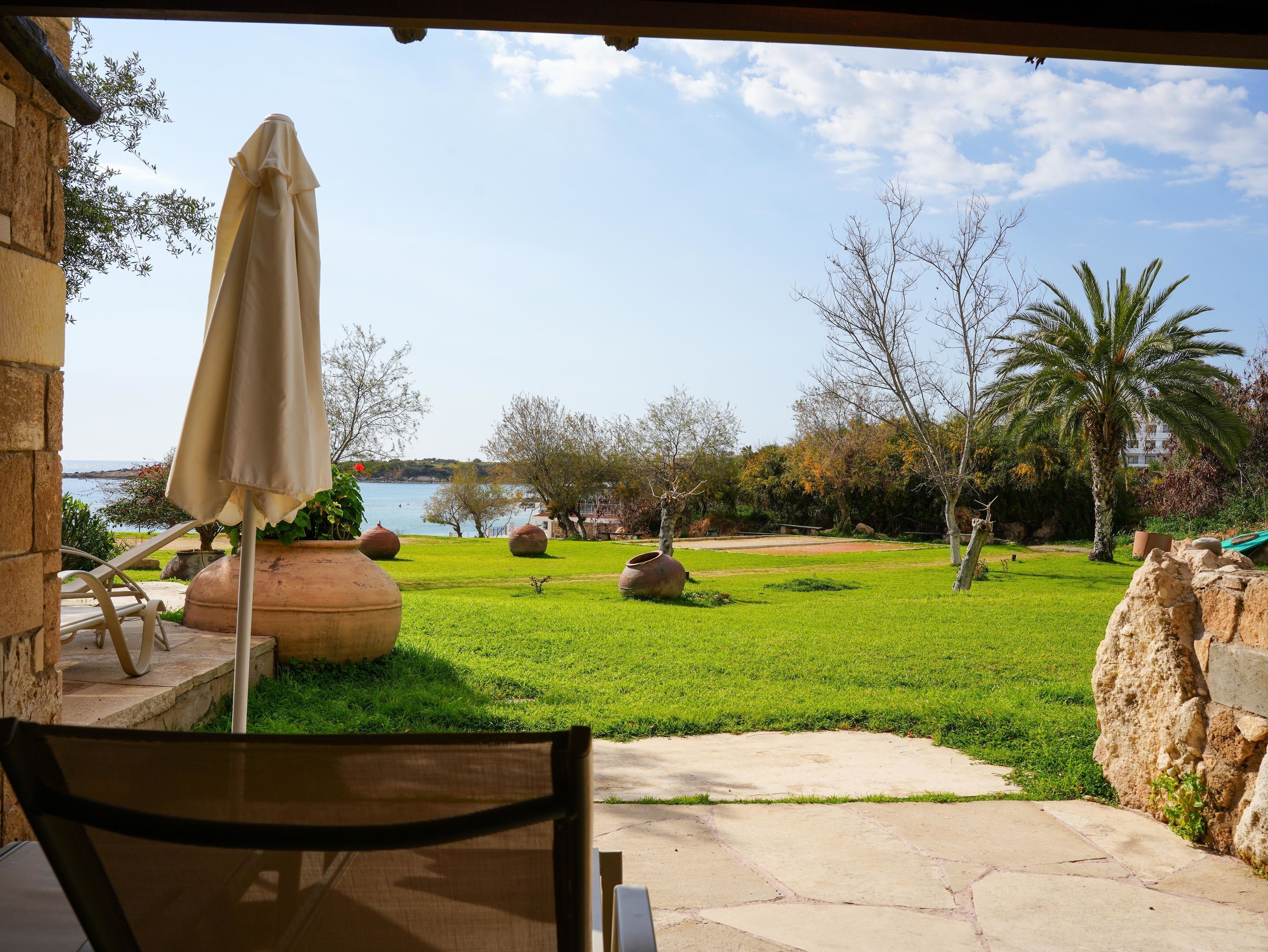 Un patio con vistas a un cuerpo de agua, mobiliario exterior y una zona verde con árboles y rocas.