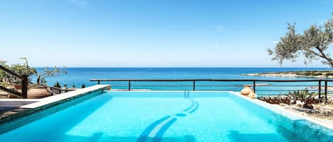 A swimming pool with a view of the sea, a stone wall, and some greenery.