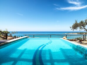 Una piscina con vistas al mar, un muro de piedra y algo de vegetación.