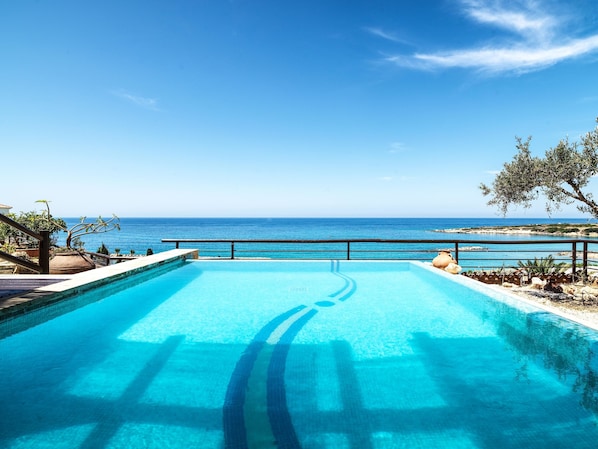 A swimming pool with a view of the sea, a stone wall, and some greenery. - Coral Beach Hotel and Resort (Pegeia)