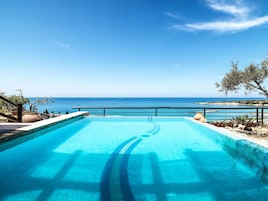 A swimming pool with a view of the sea, a stone wall, and some greenery.