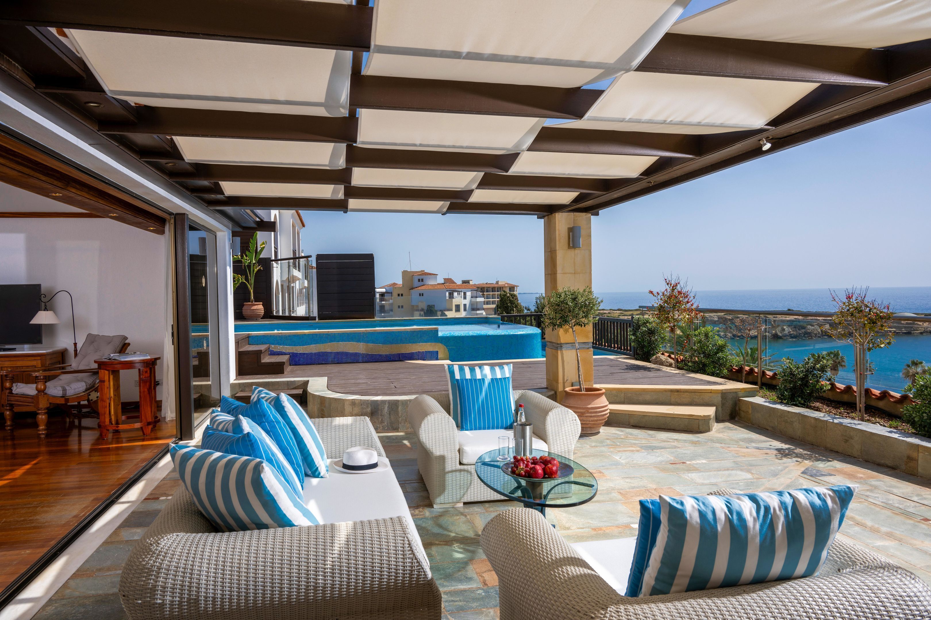 Un espace extérieur aménagé avec des meubles en osier et une table en verre, offrant une vue sur la côte, avec des bâtiments et un ciel dégagé.