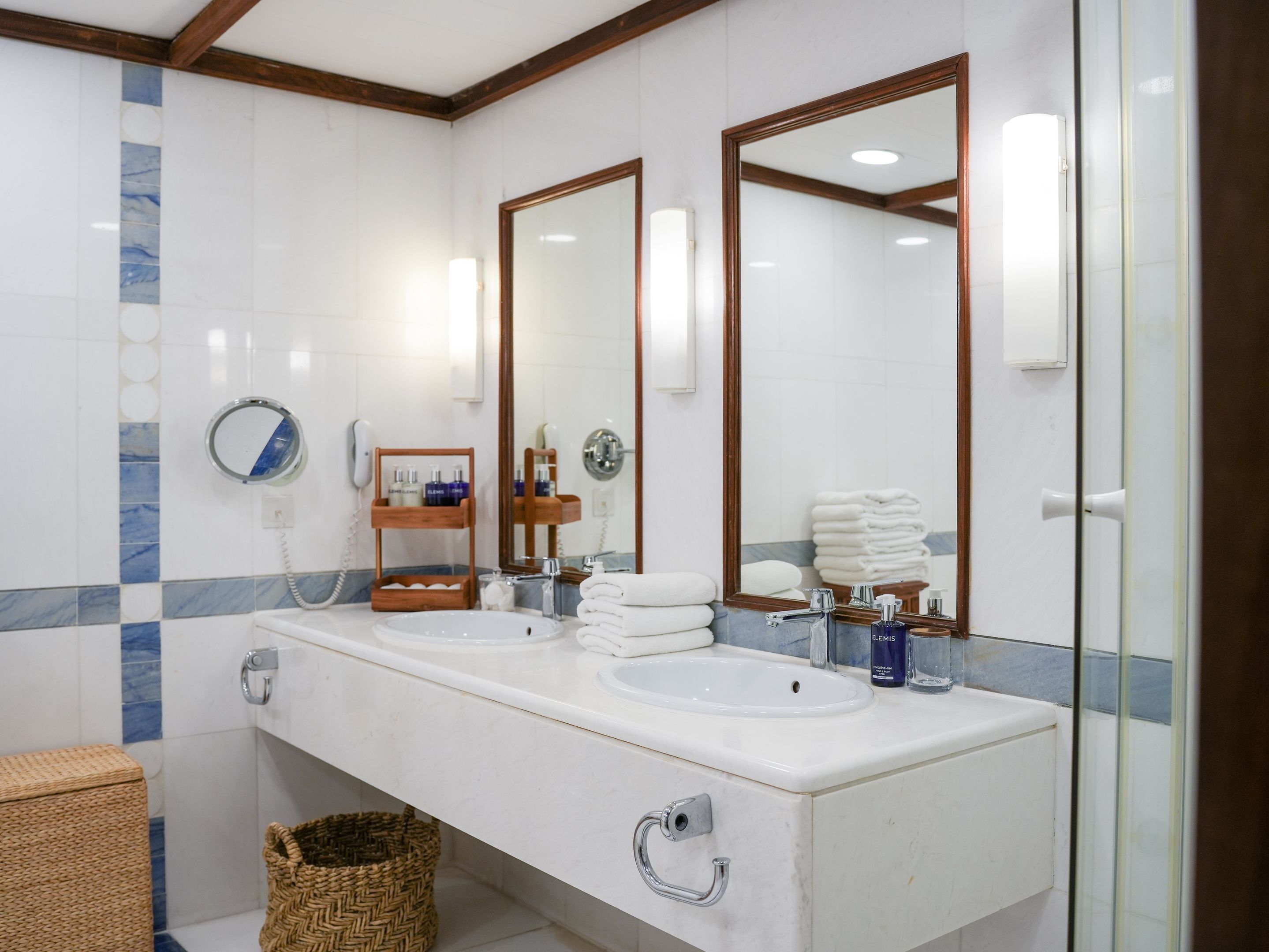A bathroom with two sinks, a mirror, a towel rack, and a wicker basket.