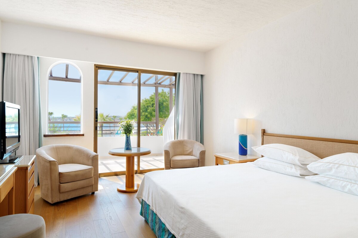 Een hotelkamer met een bed, twee stoelen, een televisie, een lamp en uitzicht op de omgeving.