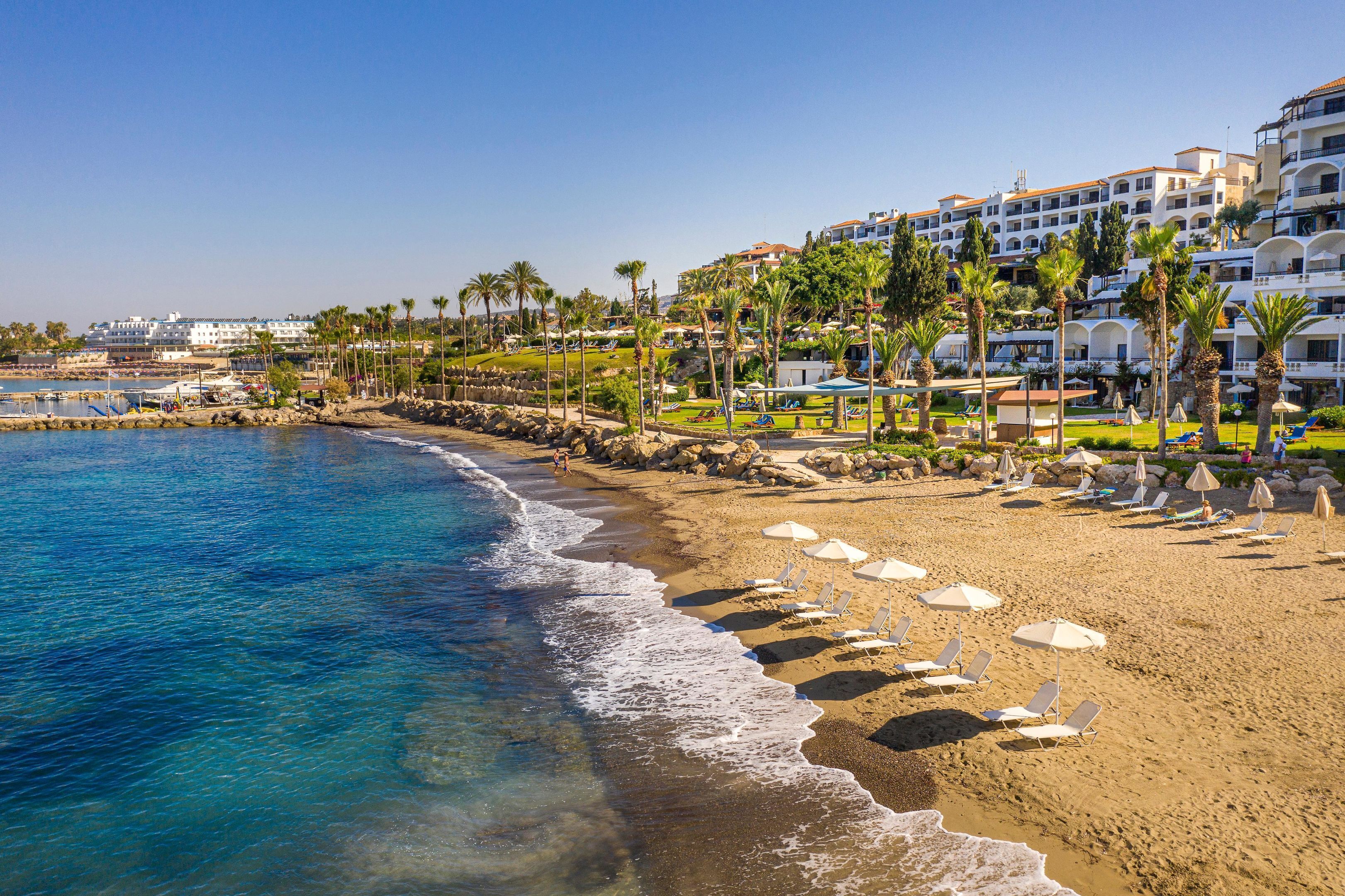 A beach resort with a sandy shoreline, palm trees, and a building with balconies overlooking the beach.