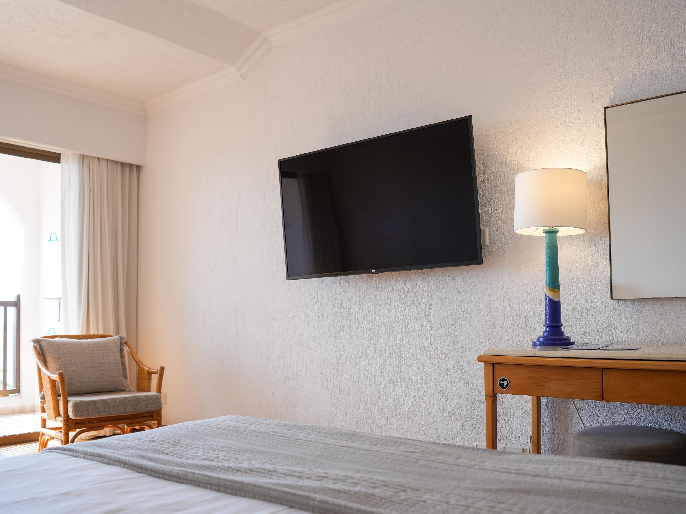 Una habitación de hotel con una cama, un televisor montado en la pared, un escritorio con una lámpara y una silla.