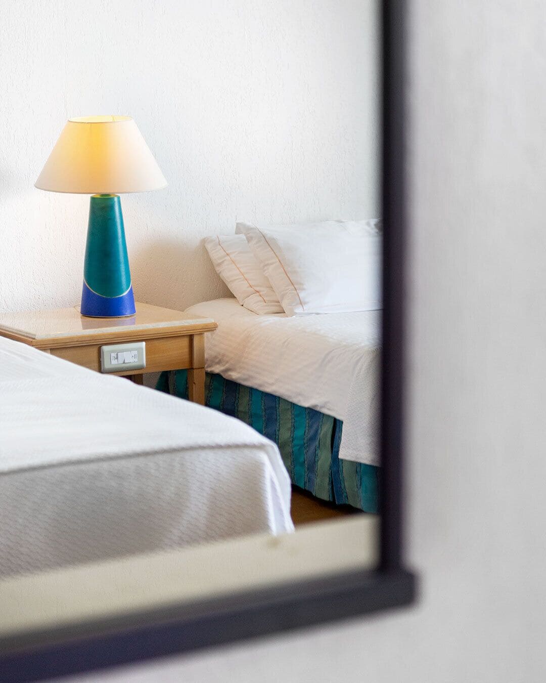 Quarto de hotel com cama, mesa de cabeceira com abajur e tomada.