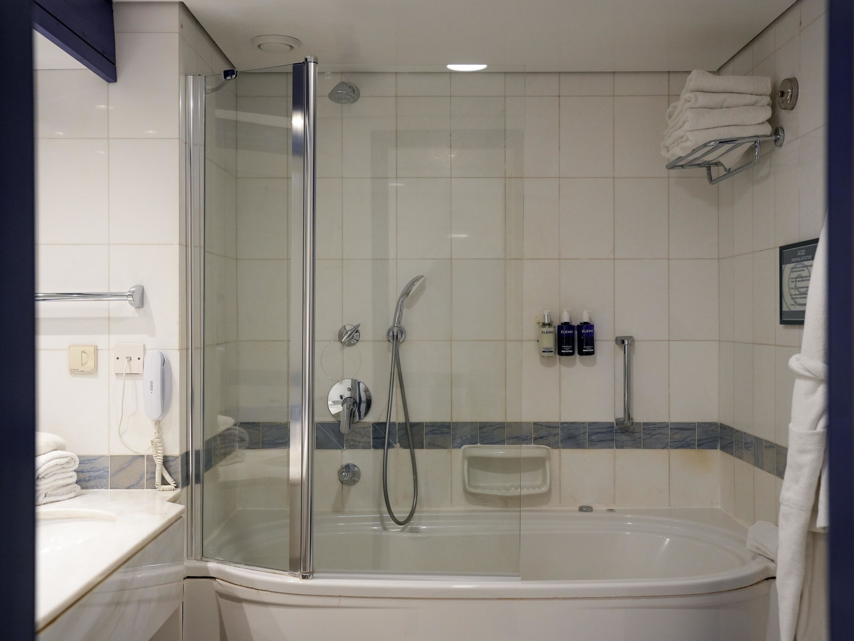 Een badkamer met een douche met glazen wand, een badkuip, een handdoekrek en toiletartikelen.