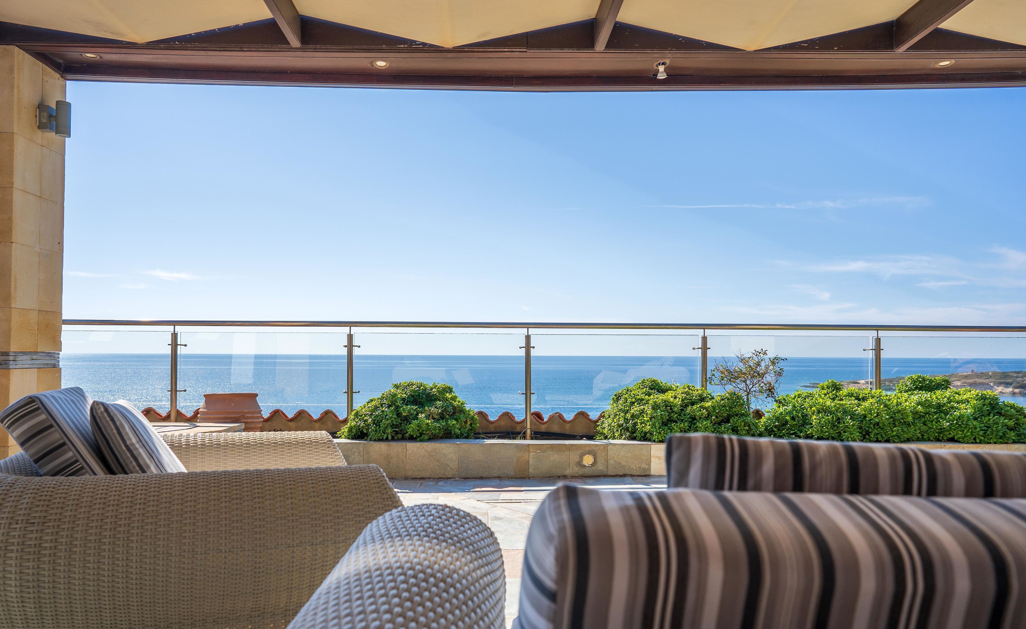 En balkon med udsigt over havet, fletmøbler og et gelænder.