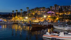 A marina with boats docked, a beach area with umbrellas, and a hotel in the background. - Coral Beach Hotel and Resort (Pegeia)