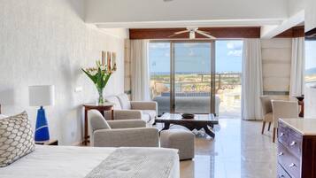 A hotel room with a bed, a seating area with chairs, a table, a vase with flowers, and a view of the ocean.