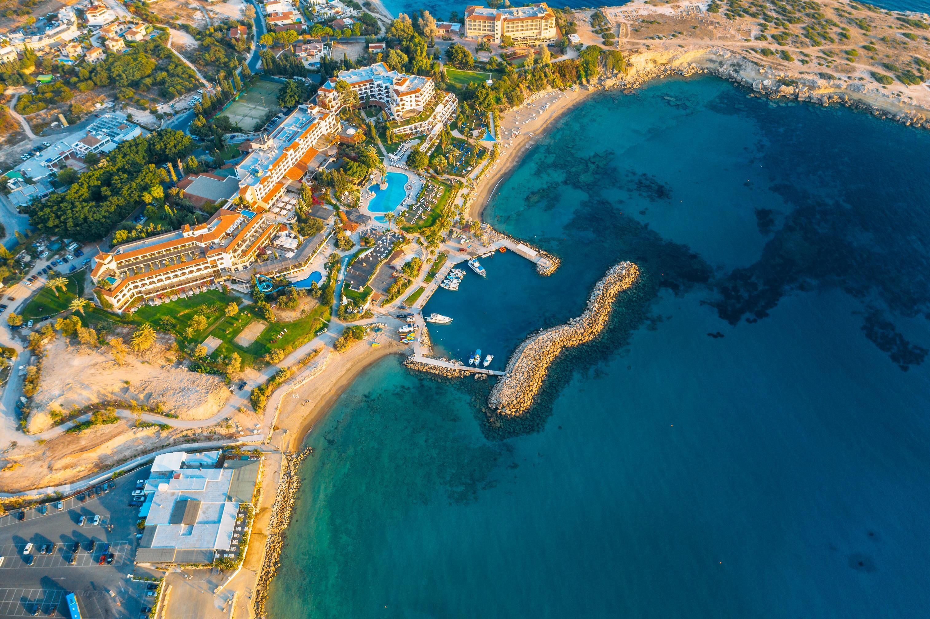 Vista aérea de un complejo turístico costero con varias edificaciones, un puerto deportivo y una playa.