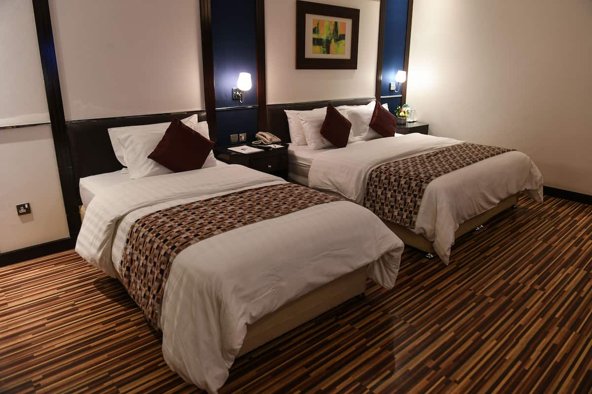 A hotel room with two beds, wooden flooring, and a nightstand with a telephone.