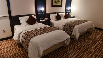 A hotel room with two beds, wooden flooring, and a nightstand with a telephone.