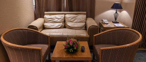 Habitación de hotel con sofá, dos sillones, una mesita con un jarrón de flores, una lámpara y un teléfono sobre una mesita auxiliar.