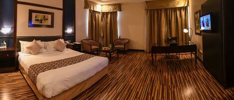 A hotel room with a large bed, two chairs, a desk, and a television.