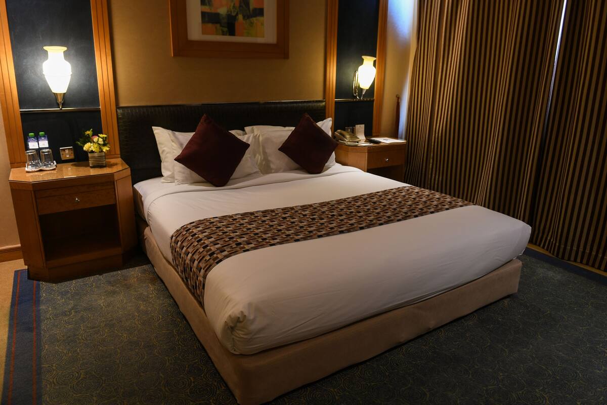 A hotel room with a large bed, two bedside tables, a nightstand, a lamp, and a curtain.