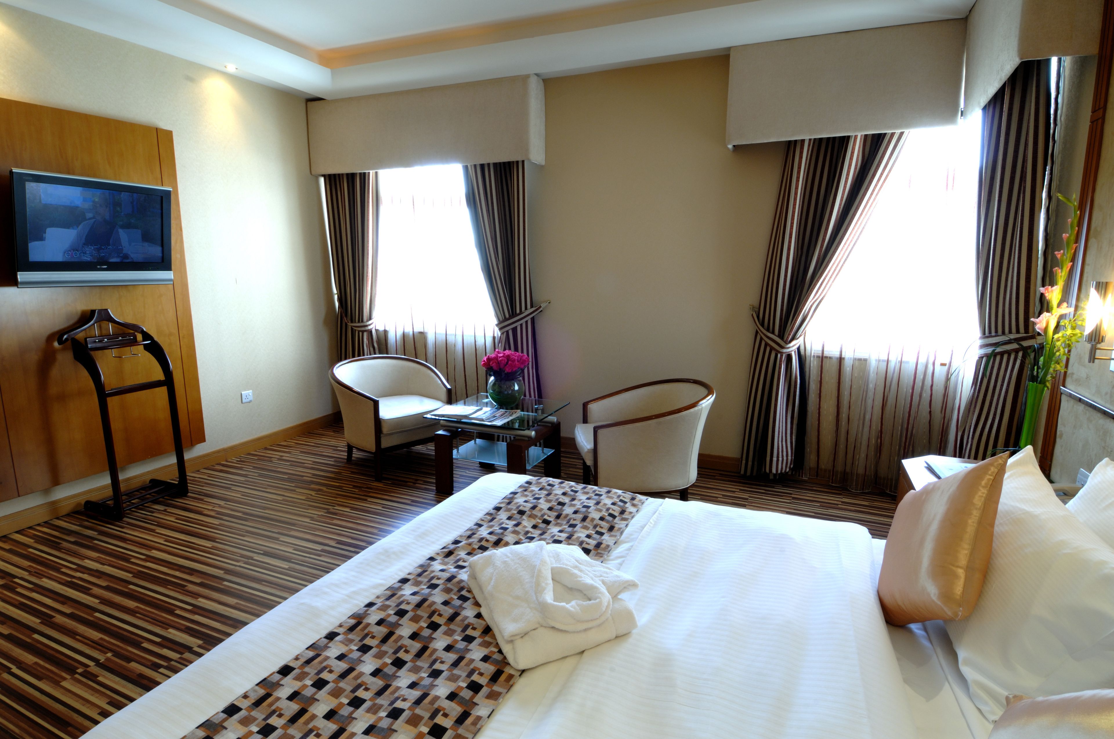 Habitación de hotel con una cama grande, dos sillas, televisión y ventana con cortinas.